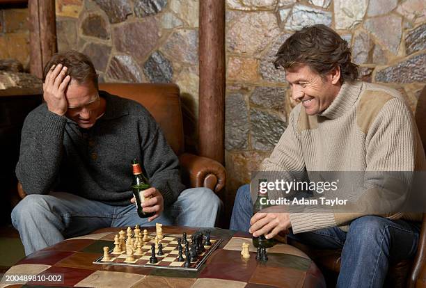 two men playing chess holding beer bottles, smiling - man cave stock-fotos und bilder