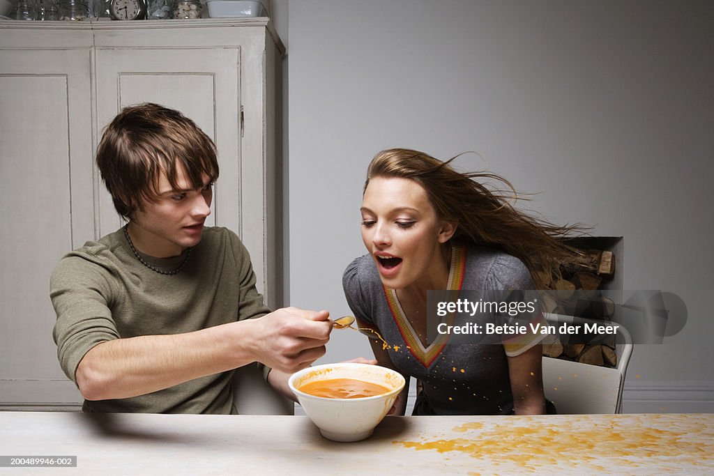 Couple trying to eat soup as strong gust of wind blows through kitchen