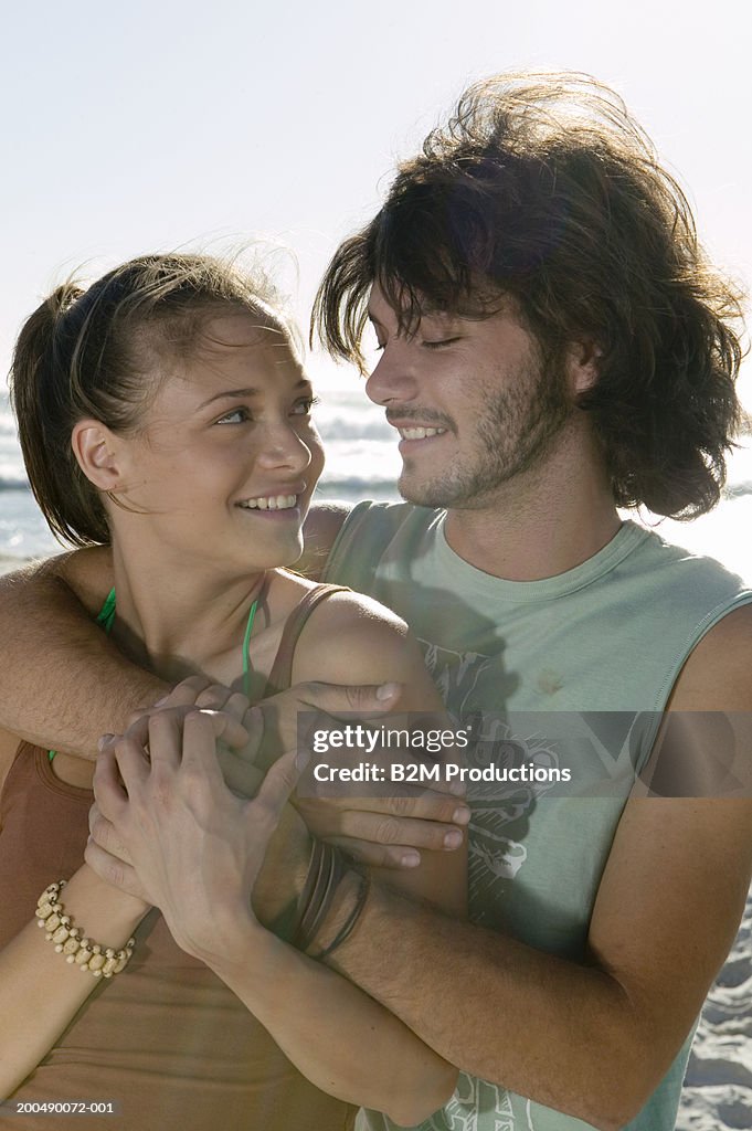 Young couple embracing on beach, looking at each other, smiling