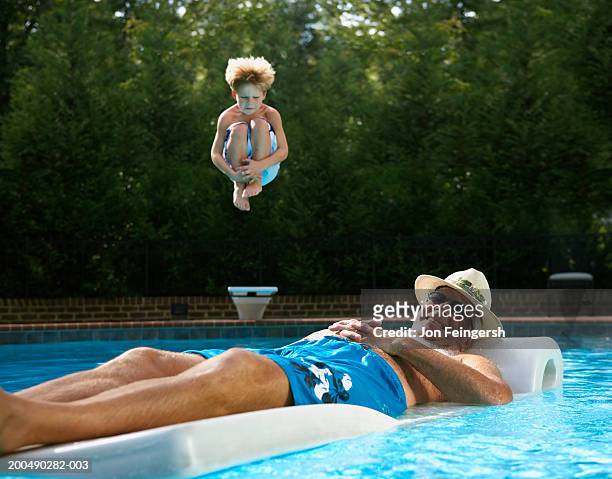 senior man on float in pool, boy (5-7) jumping in - senior adult stock-fotos und bilder