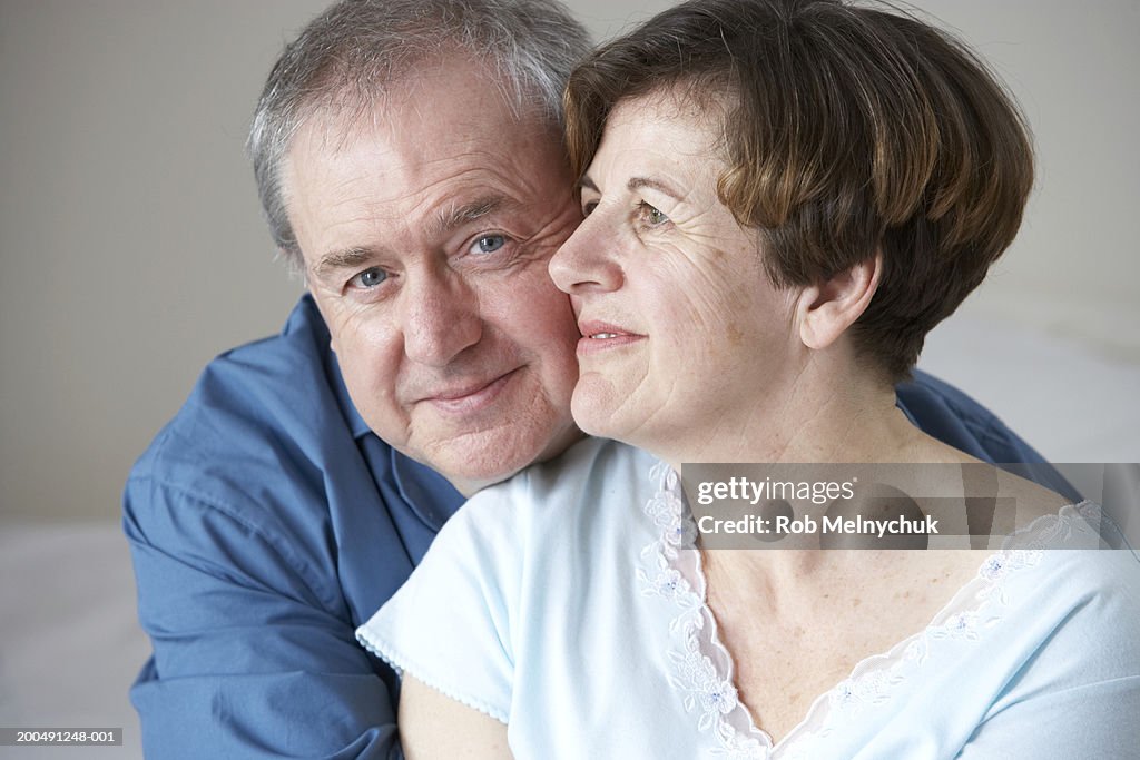 Mature man and woman embracing on bed, smiling