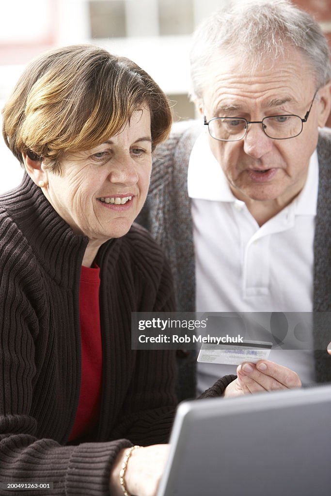 Mature man and woman holding credit card and using laptop