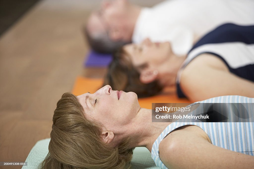 Three mature adults in yoga class (focus on woman lying in foreground)