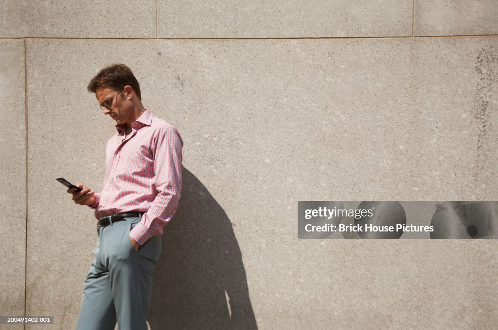 Businessman using mobile phone, standing beside wall, outdoors