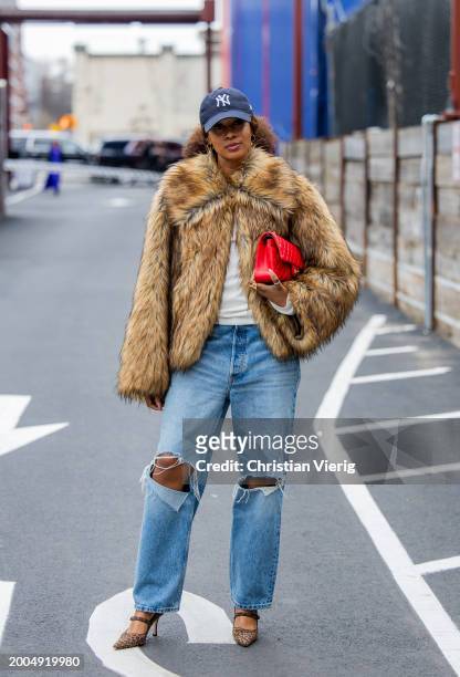 Naomi Elizee wears cap, red Chanel bag, fur jacket, ripped denim jeans outside Ulla Johnson on February 11, 2024 in New York City.