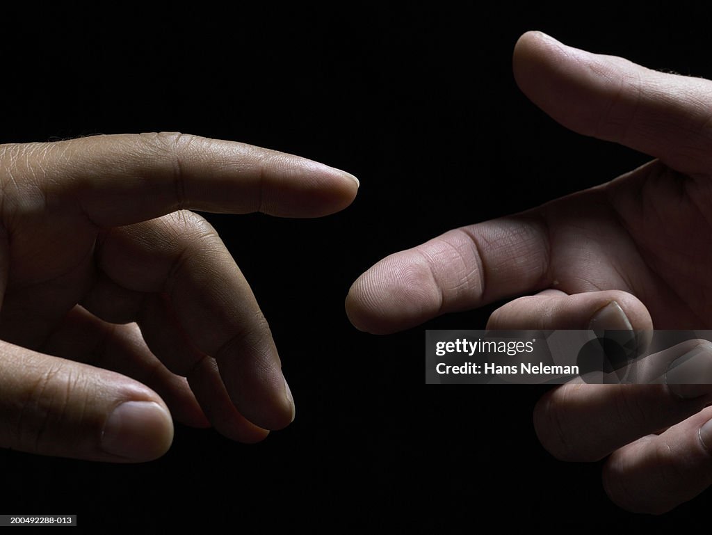 Two hands reaching out, fingers about to touch, close-up, side view