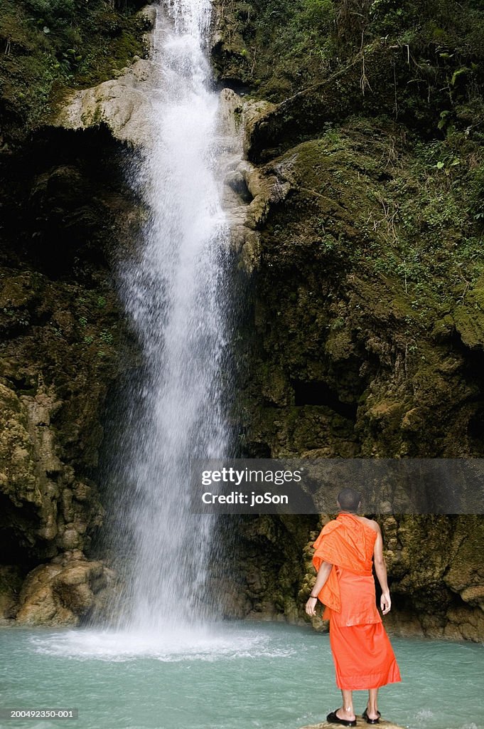 Laos, Luang Prabang, Buddhist monk facing falls, rear view