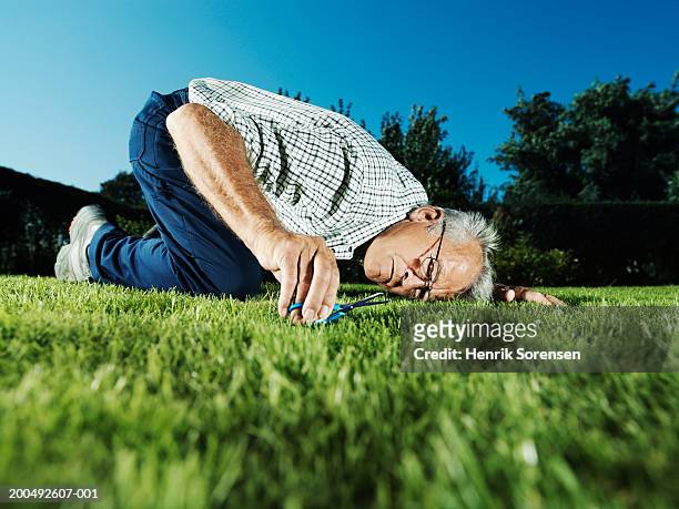 senior man cutting grass with scissors, ground view - schere stock-fotos und bilder