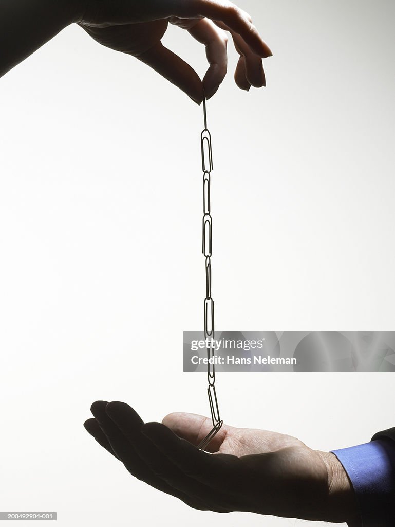 Woman placing paper clip chain in palm of man's hand, side view