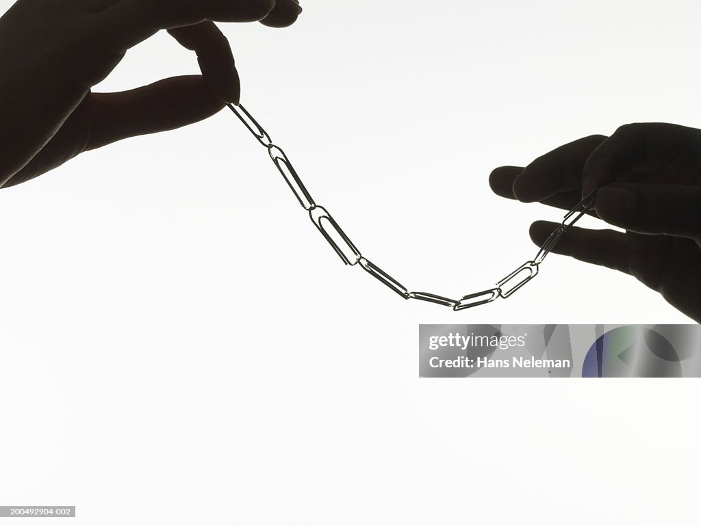 Man and woman holding paper clip chain in tips of fingers, close-up
