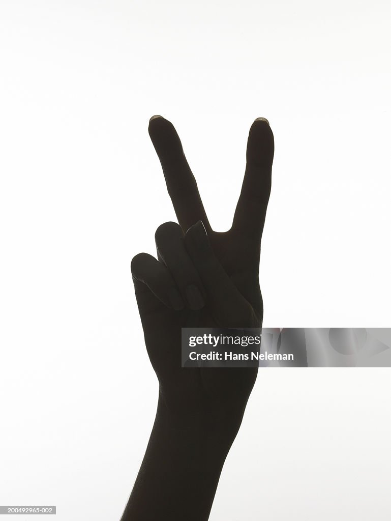Woman making 'peace' hand sign, close-up (silhouette)