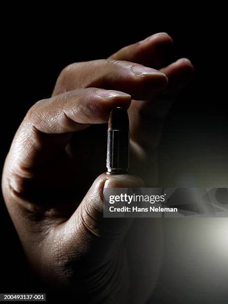 man holding single bullet between thumb and forefinger, close-up - kogel stockfoto's en -beelden