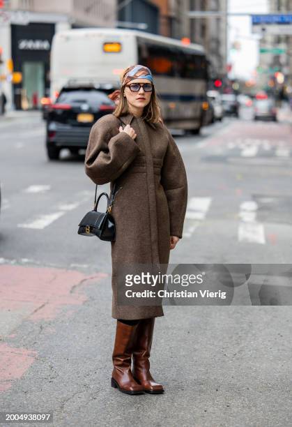 Guest wears brown tailored coat, hair scarf, black Balenciaga bag, brown bootsoutside Altuzarra on February 11, 2024 in New York City.