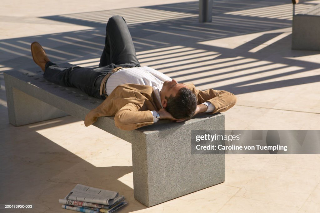 Businessman lying on bench, rear view