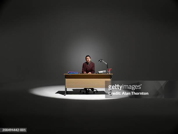 businessman sitting at desk in spotlight, looking upwards - desk stock pictures, royalty-free photos & images