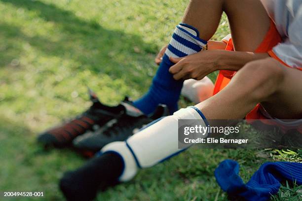 boy (10-12) putting on socks and shin guards at side of football pitch - shin guard stock pictures, royalty-free photos & images
