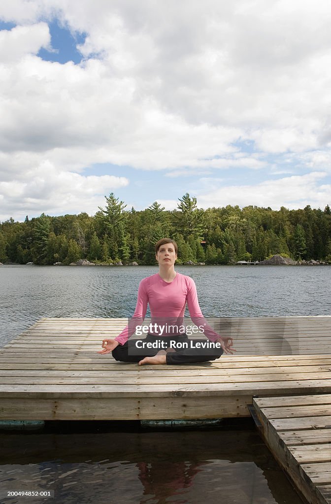 Woman meditating on jetty by lake, front view