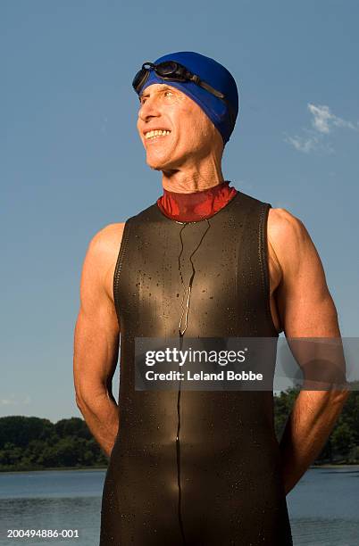 senior man in wetsuit and swimming cap standing at edge of lake - swimming cap stock pictures, royalty-free photos & images