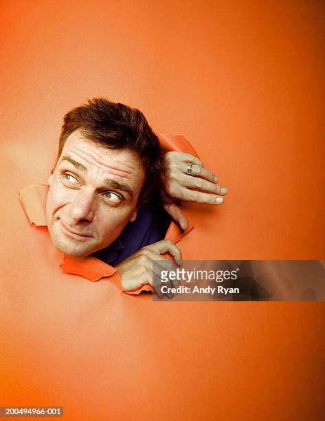 man sticking head through hole in orange wall, looking sideways - appear photos et images de collection