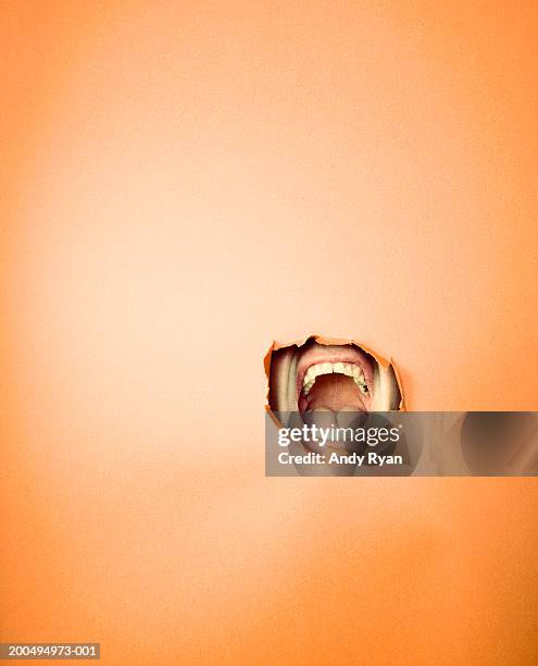 man shouting through hole in orange wall, view of open mouth - mouth open stock-fotos und bilder