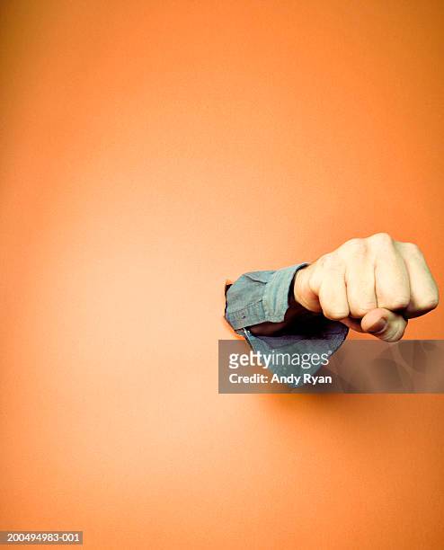 man punching hole in orange wall, close-up of fist - appearance foto e immagini stock