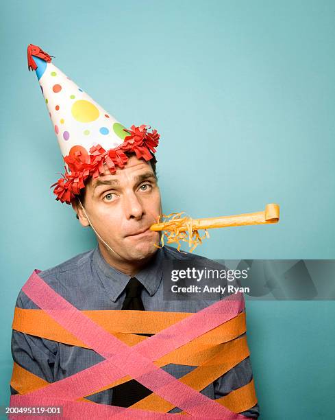 man wearing party hat tied up in ribbons, blowing party blower - party horn blower stock pictures, royalty-free photos & images