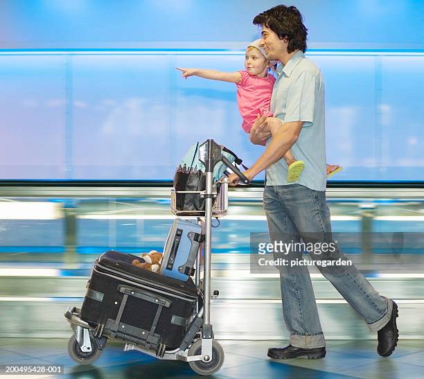 father carrying daughter (2-4) and pushing luggage trolley, side view - luggage trolley stock pictures, royalty-free photos & images