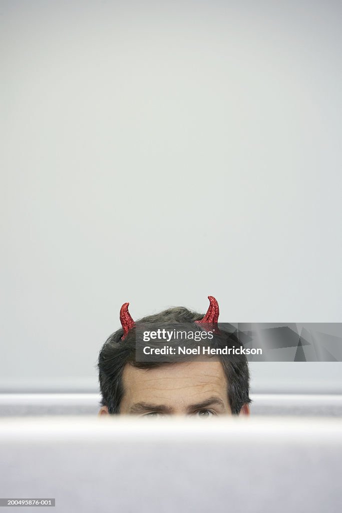 Mature businessman with devil horns sitting in cubicle, high section