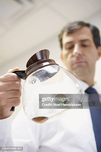 mature businessman holding empty coffee pot in office kitchen - coffee pot stock pictures, royalty-free photos & images