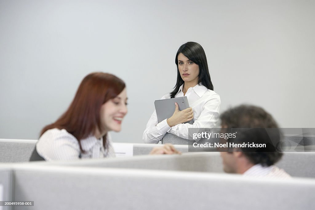 Businesswoman watching two coworkers talking over cubicle wall