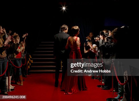 Celebrity couple in evening wear walking on red carpet, rear view Celebrity couple in evening wear walking on red carpet, rear view