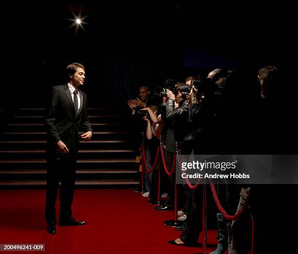 male celebrity in tuxedo standing on red carpet in front of paparazzi - red carpet foto e immagini stock