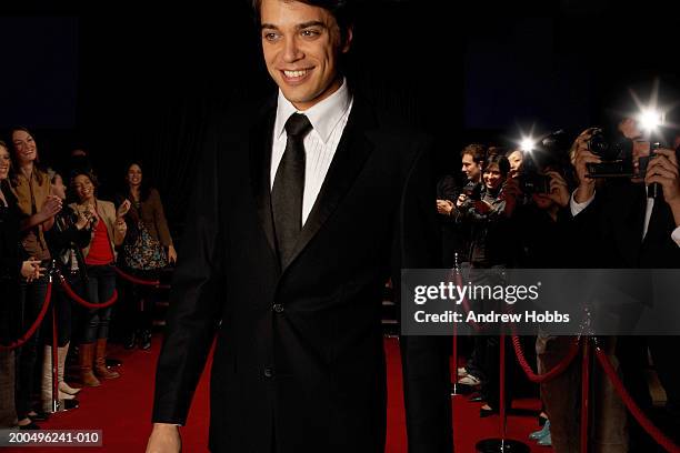 male celebrity in tuxedo walking on red carpet past paparazzi and fans - red suit stockfoto's en -beelden