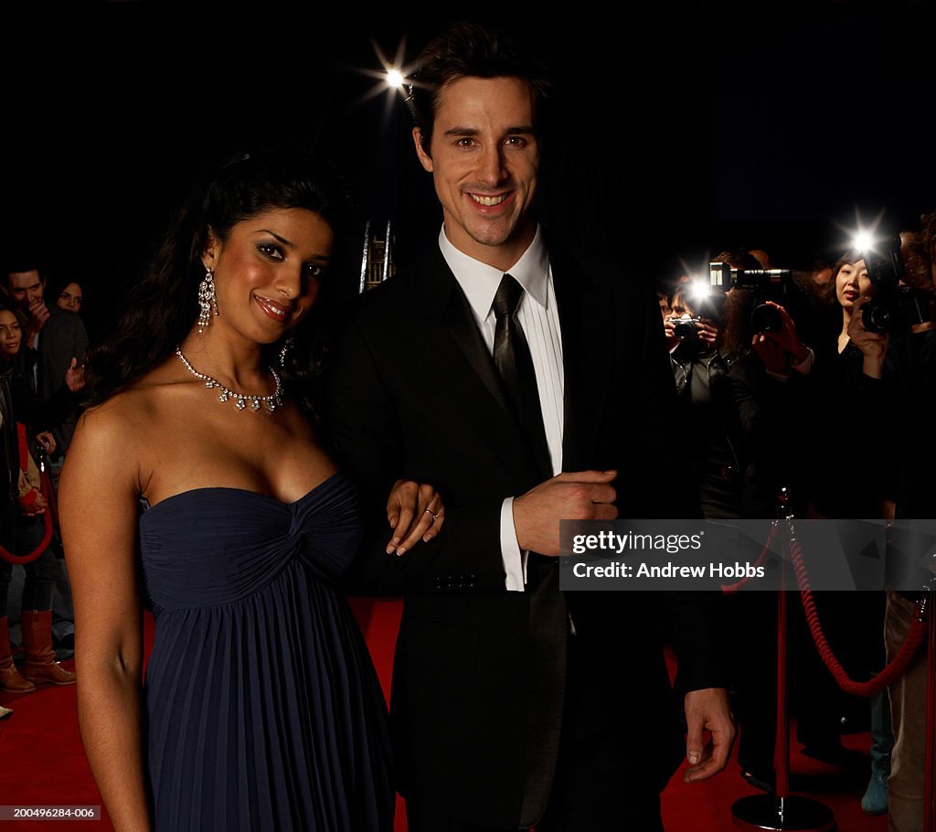 Paparazzi photographing celebrity couple in evening wear on red carpet