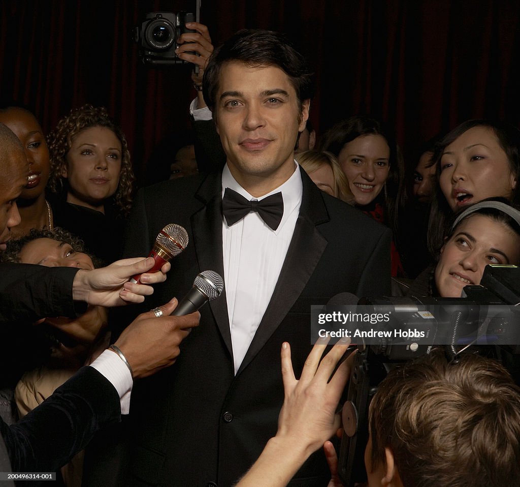 Celebrity male in tuxedo talking to fans and media at event, portrait