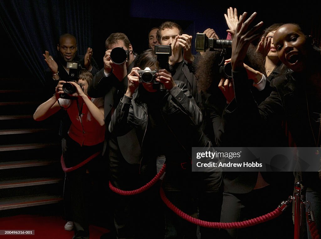 Paparazzi and excited fans standing behind rope barrier on red carpet