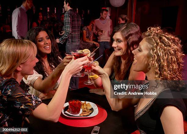 four young women sitting in bar with cocktails, making toast, smiling - 4 cocktails stockfoto's en -beelden