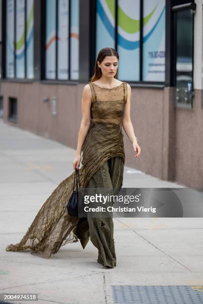Guest wears transparent asymmetric dress, khaki olive green pants, black bag outside Jason Wu on February 11, 2024 in New York City.