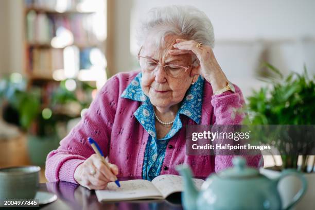 portrait of elderly woman solving sudoku puzzles at home, sitting in living room. sudoku as popular game for aging people, logical thinking, problem solving. - alzheimer fotografías e imágenes de stock