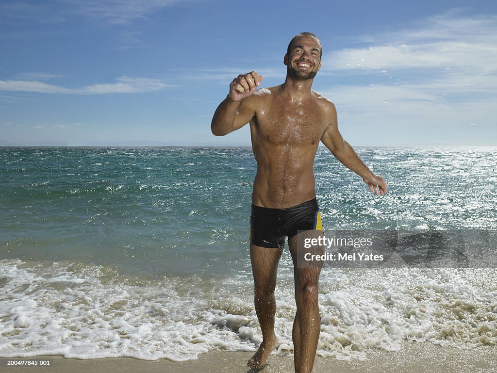 Young man walking out of sea on beach, close-up