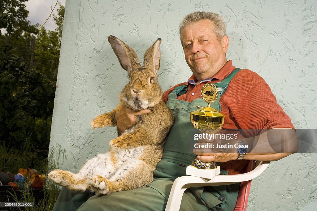Man holding large rabbit and trophy, outside