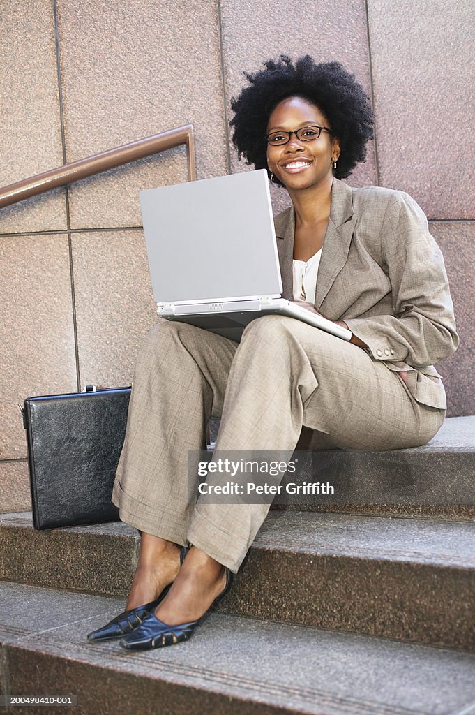 Businesswoman sitting on steps, using laptop