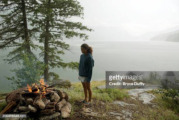 young woman standing by campfire during rainstorm - slocan lake stock pictures, royalty-free photos & images
