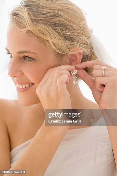 young bride putting on diamond earrings, smiling, close-up - woman putting on diamond stock pictures, royalty-free photos & images