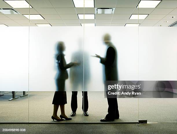 three colleagues standing behind frosted glass in office, talking - frosted glass stockfoto's en -beelden
