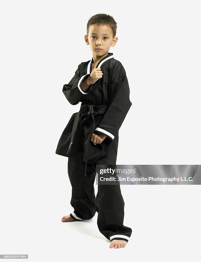 Boy (6-8) in karate outfit striking kicking pose