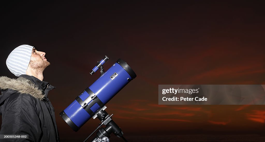 Young man with telescope looking at sky, dusk, side view