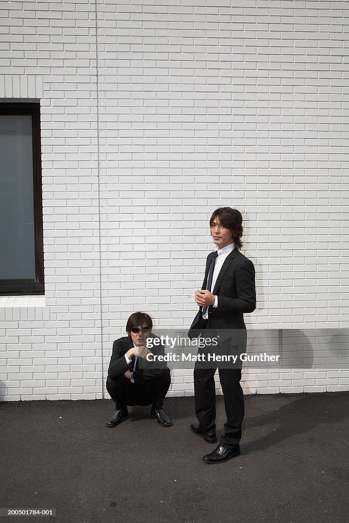 Two businessmen beside brick wall outdoors