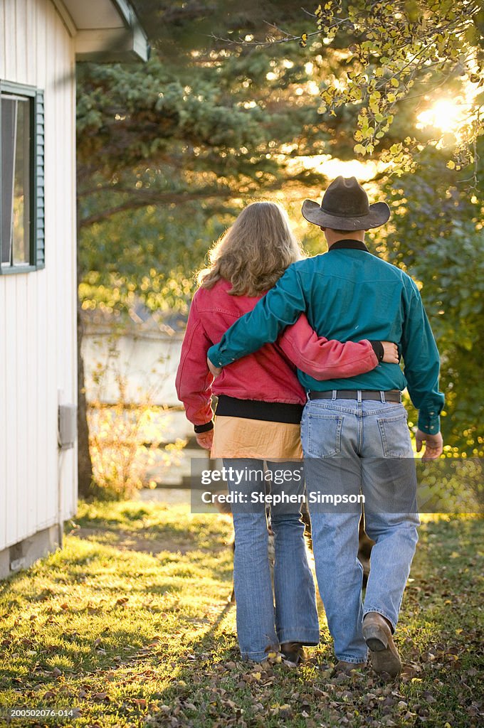 Young couple walking in garden, arm around one another, rear view