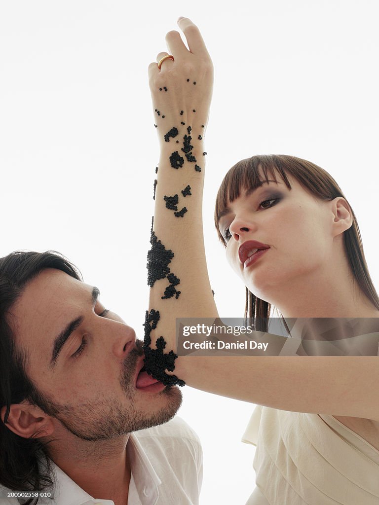 Man licking caviar off of woman's arm, indoors